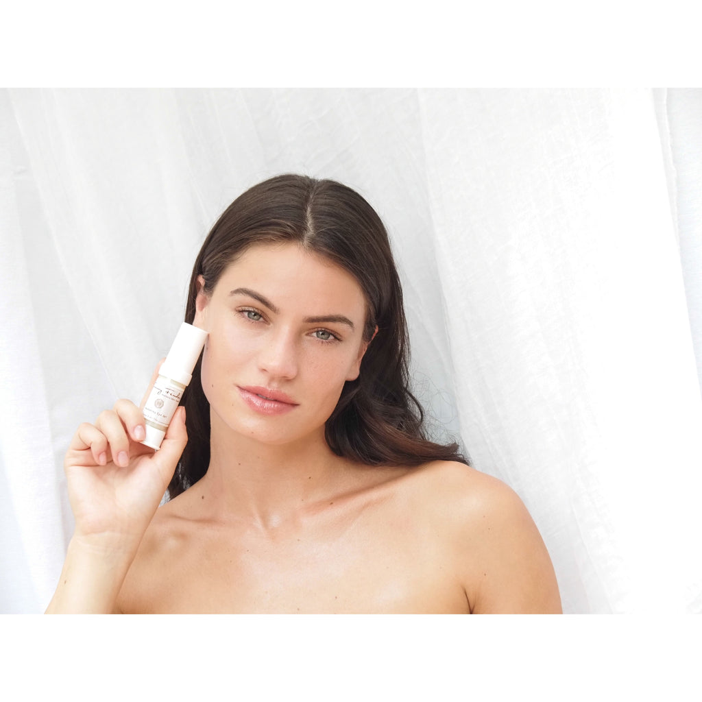 Woman holding a skincare product with a subtle smile against a white background.