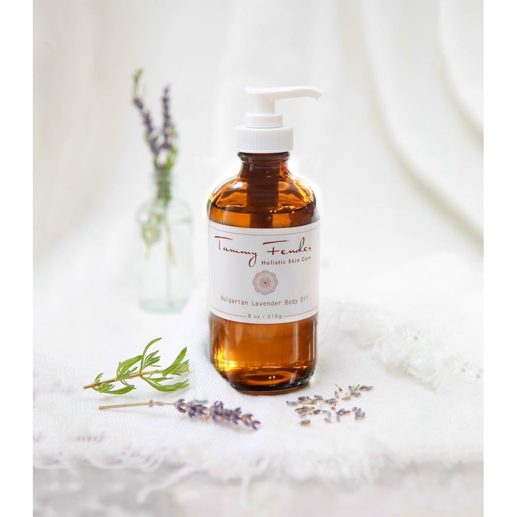 Amber glass bottle with pump containing lavender skincare product, accompanied by fresh and dried lavender sprigs on a white backdrop.