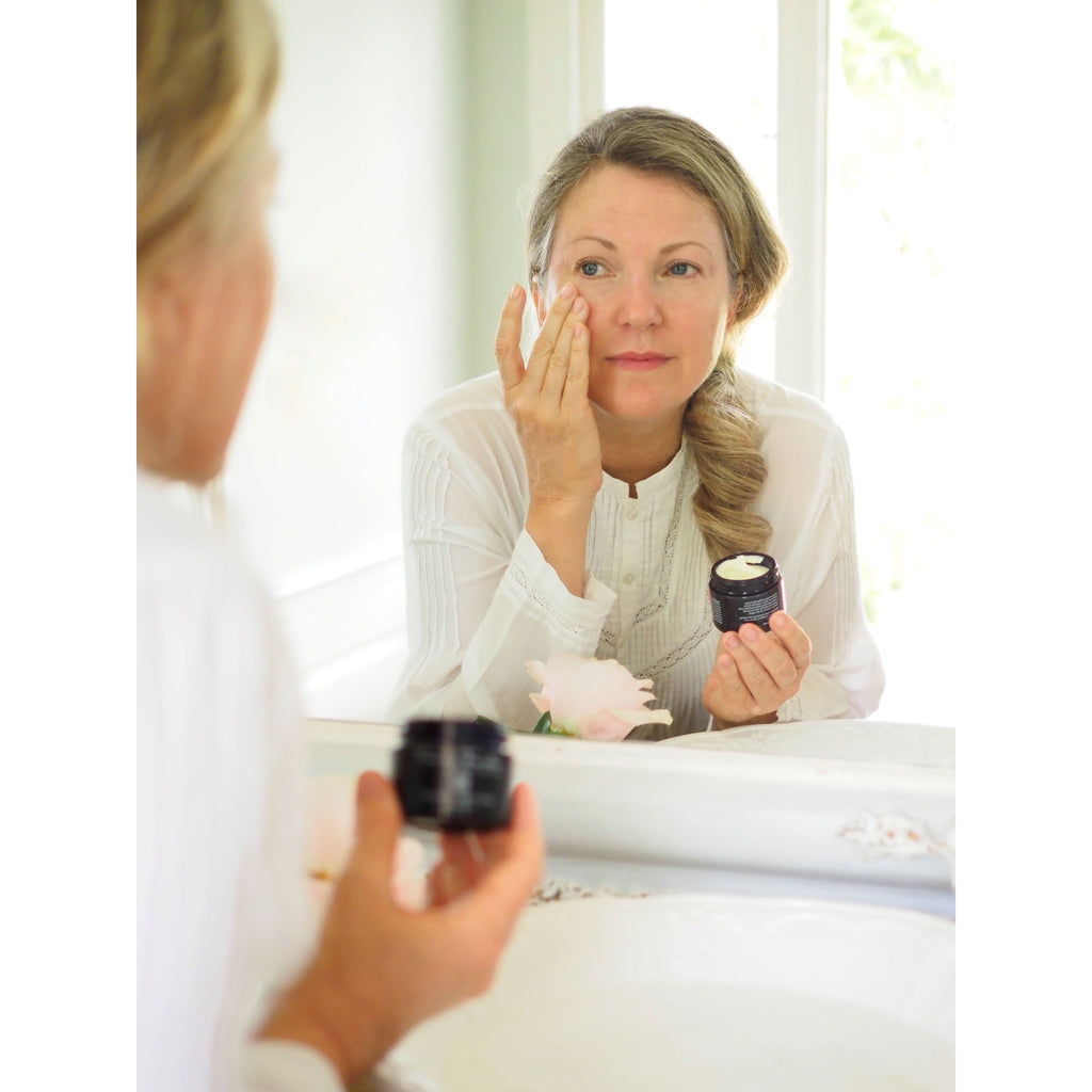 Woman applying cream to her face while looking into a mirror.