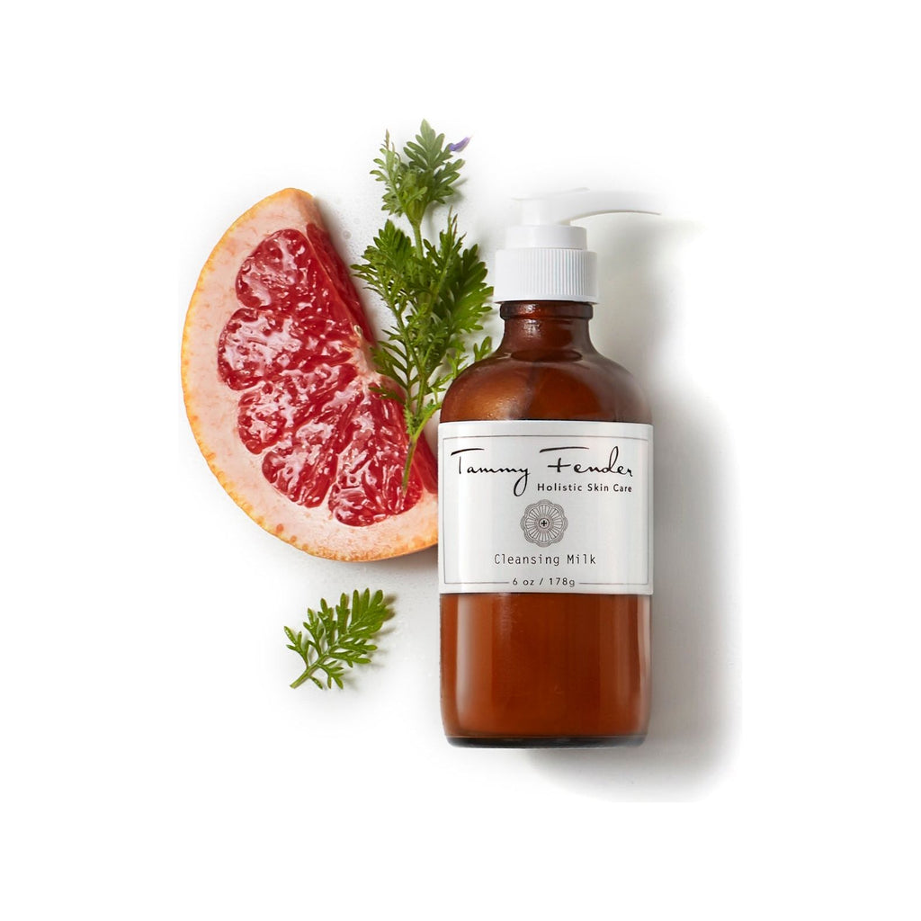 Bottle of cleansing milk with grapefruit and herbs on a white background.