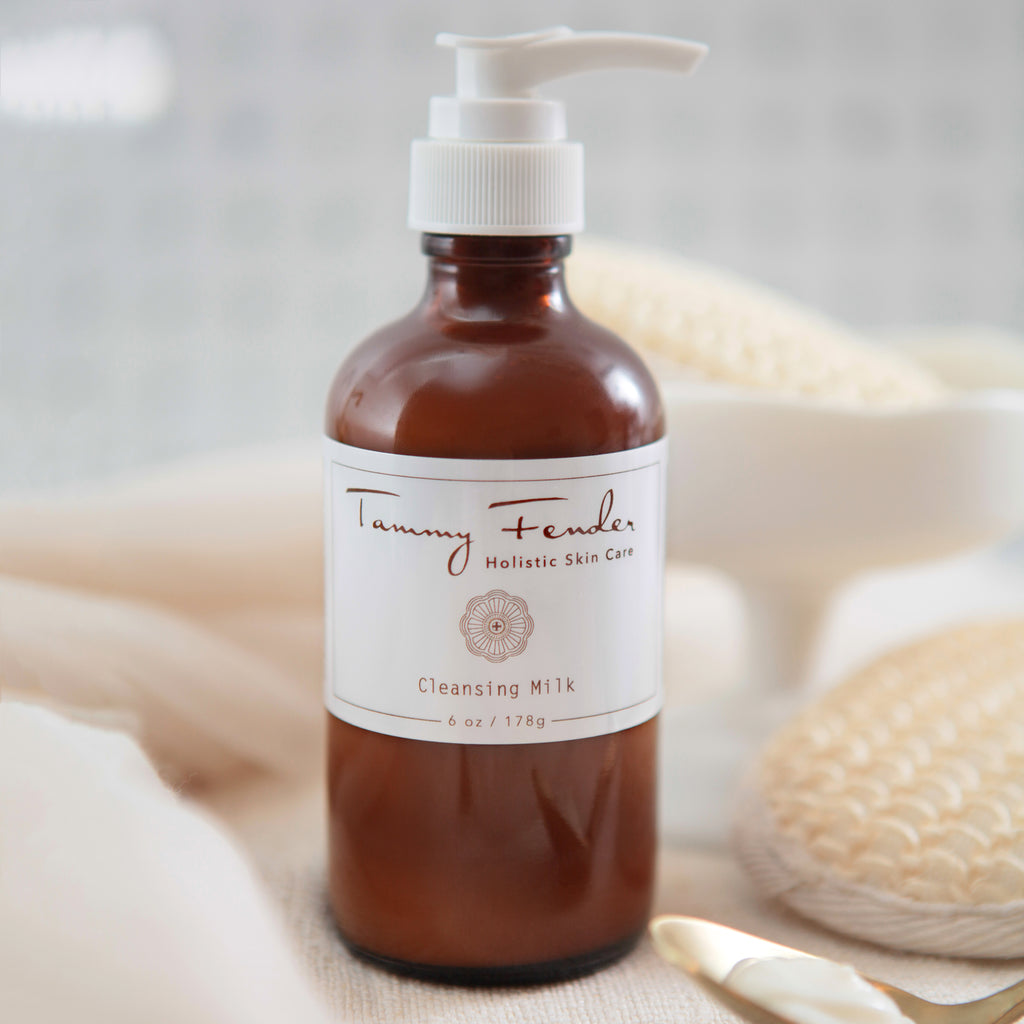 Brown glass bottle with white label containing cleansing milk, accompanied by spa accessories.