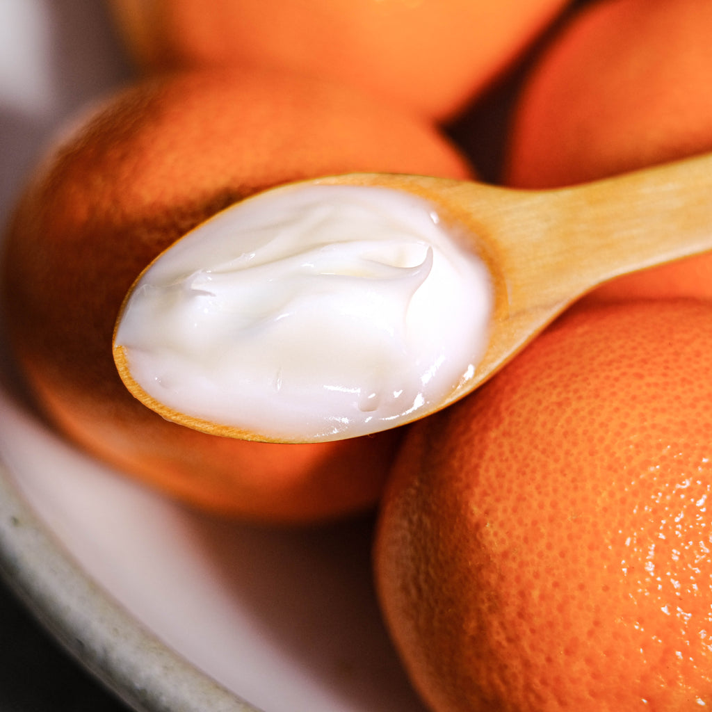 A wooden spoon holding yogurt with oranges in the background.