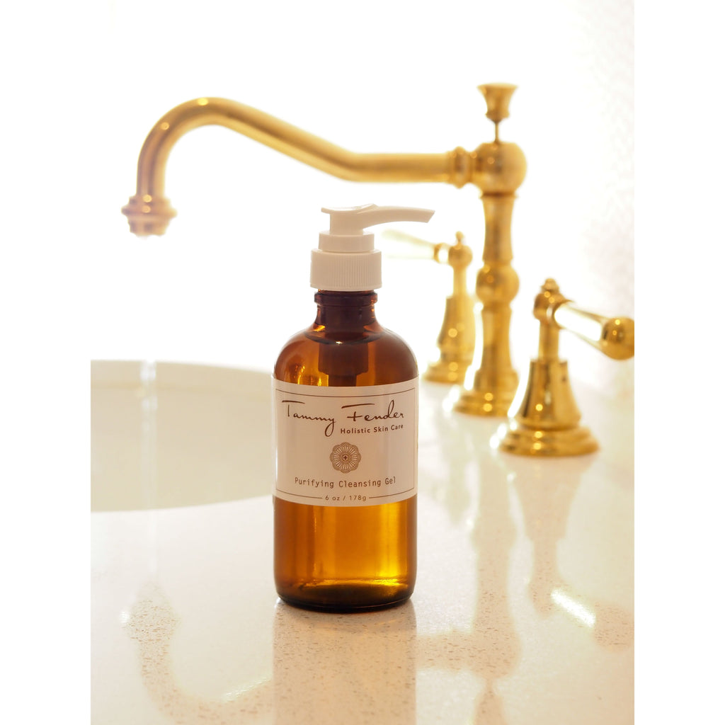 Amber glass bottle of cleansing oil on a bathroom counter with gold faucets in the background.