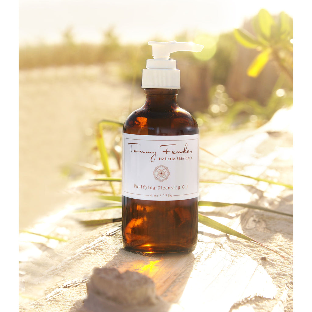 Amber bottle of purifying cleansing gel on a sandy beach with sunlight in the background.
