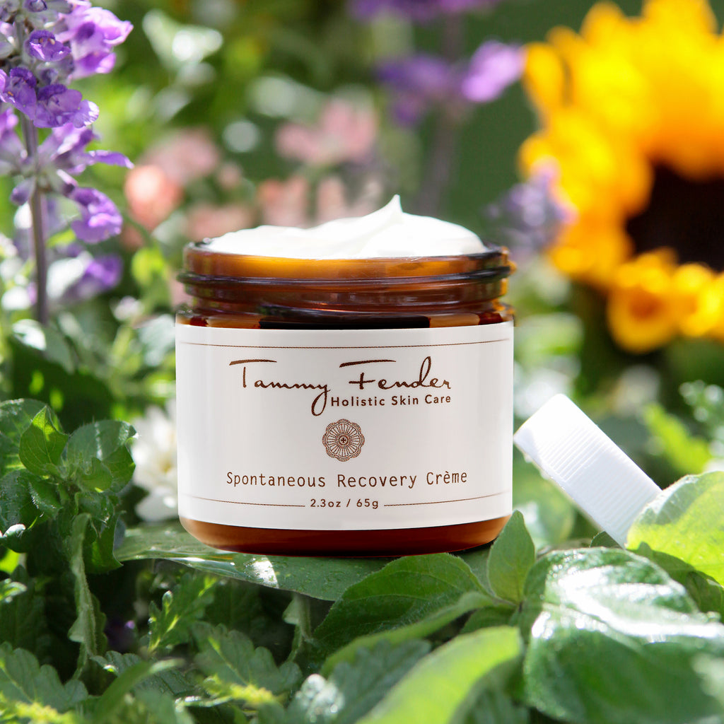 Jar of holistic skin care cream surrounded by colorful flowers.