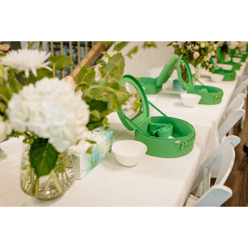 Elegant table setting with green caddies containing dining utensils, alongside white floral arrangements on a white tablecloth.