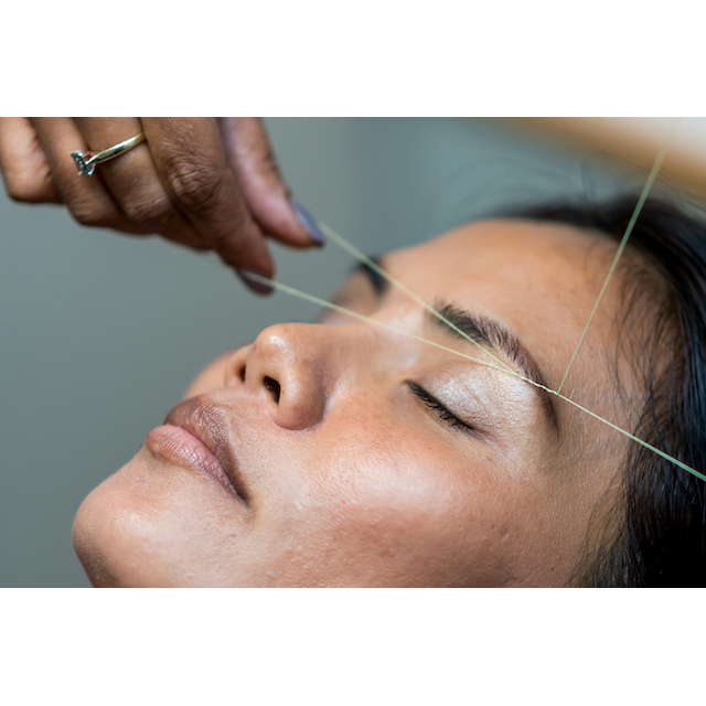 A woman receiving Threading For Brow and Face treatment from skilled estheticians, focusing on the precise removal of unwanted facial hair using a thread.