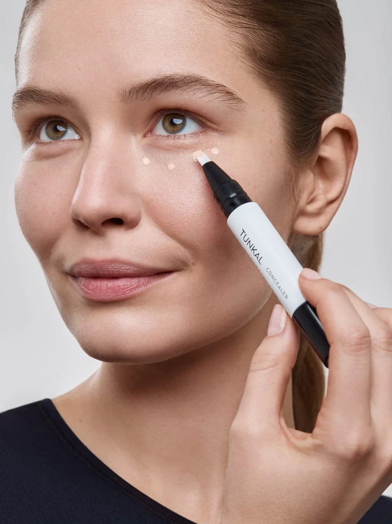 Model applying Brightening concealer with flexible coverage. PORCELAIN 01: Light beige whose rosé-colored pigment components even out light to medium skin tones.