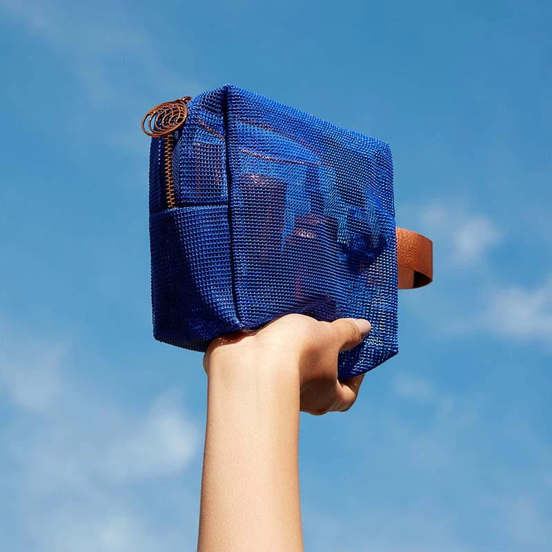 A hand holding a blue cube-shaped bag against a clear blue sky.