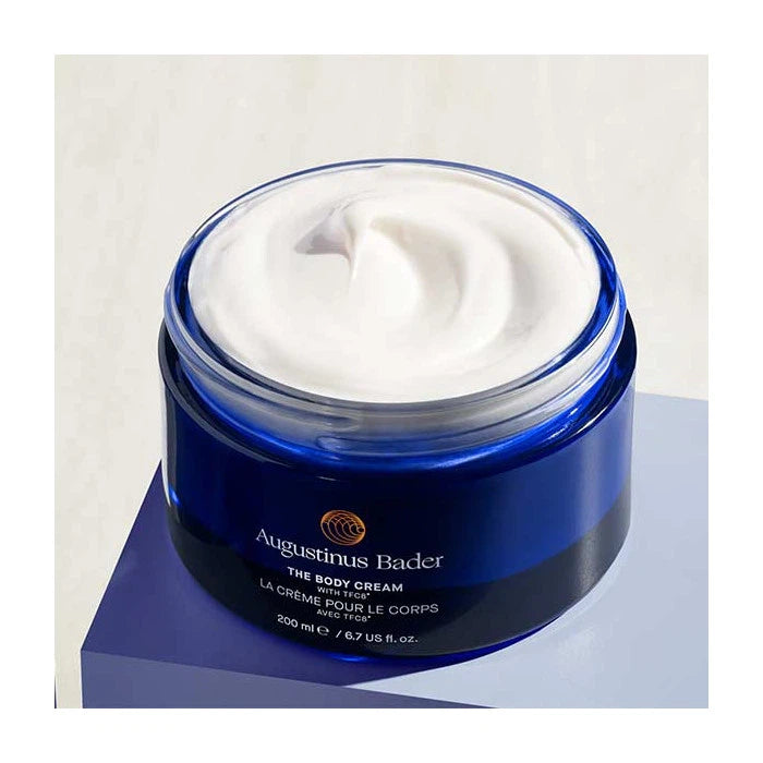 Jar of augustinus bader body cream with the lid off, revealing the creamy product inside.