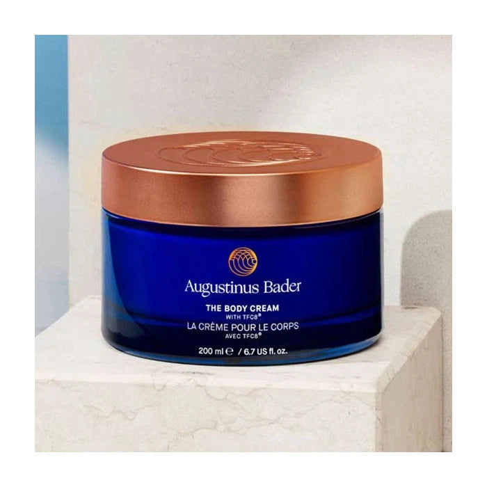 A jar of augustinus bader the body cream placed on a marble surface.