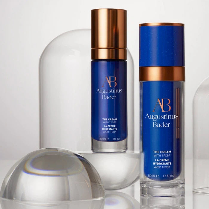 Luxury skincare products by augustinus bader on a sleek, reflective surface.
