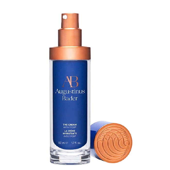 A bottle of augustinus bader skincare cream with a copper-toned dispenser and a matching cap, isolated on a white background.