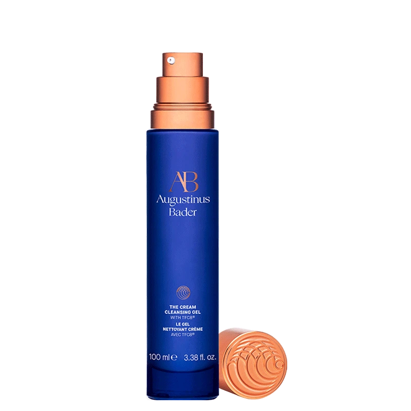 A blue bottle of augustinus bader facial cleansing gel with a copper-colored cap beside it, indicating a 100 ml capacity.
