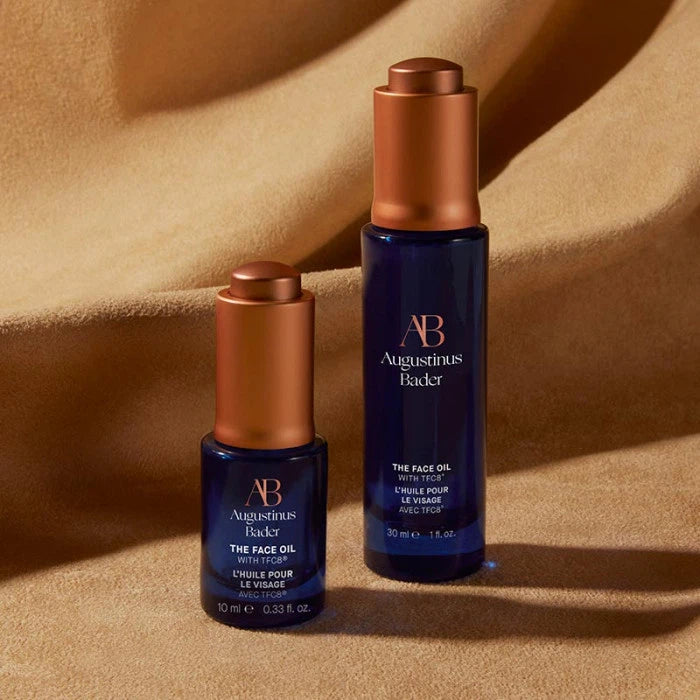 Two augustinus bader skincare bottles on a draped beige background.
