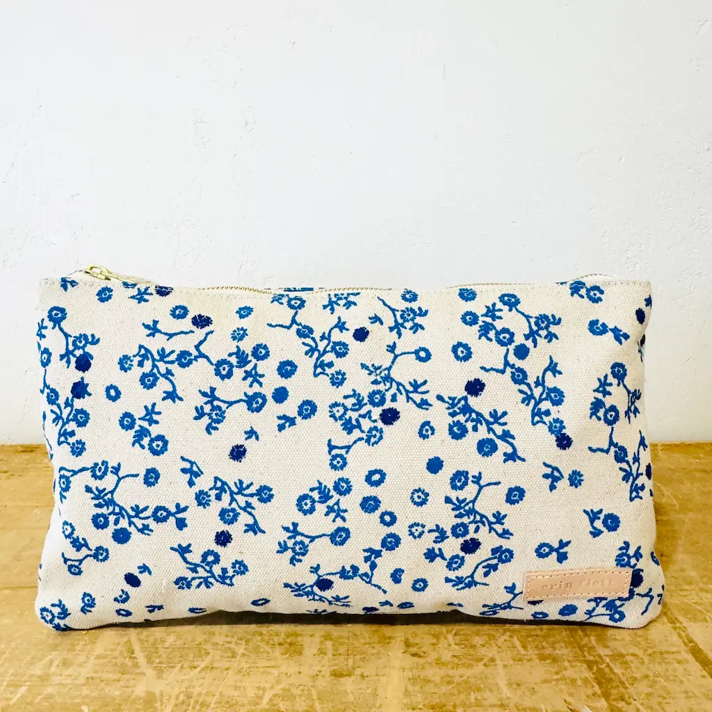 A blue floral patterned fabric pouch on a wooden surface against a white wall.