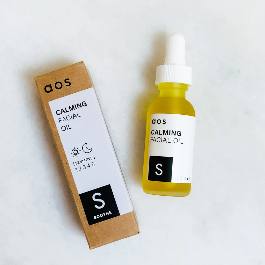 A bottle of calming facial oil next to its packaging on a white surface.
