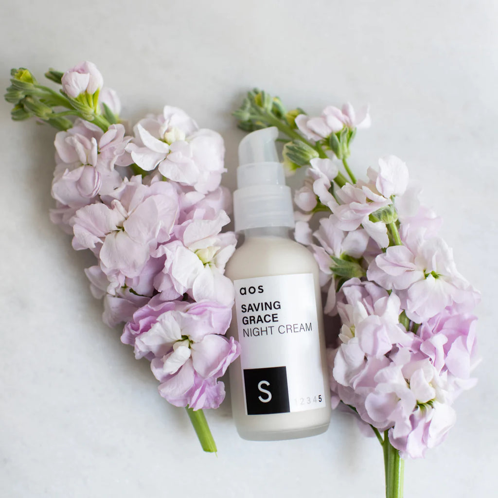 Night cream bottle surrounded by light pink flowers on a white background.