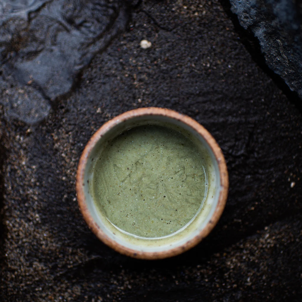 A ceramic bowl containing green matcha tea, set against a dark, textured background.