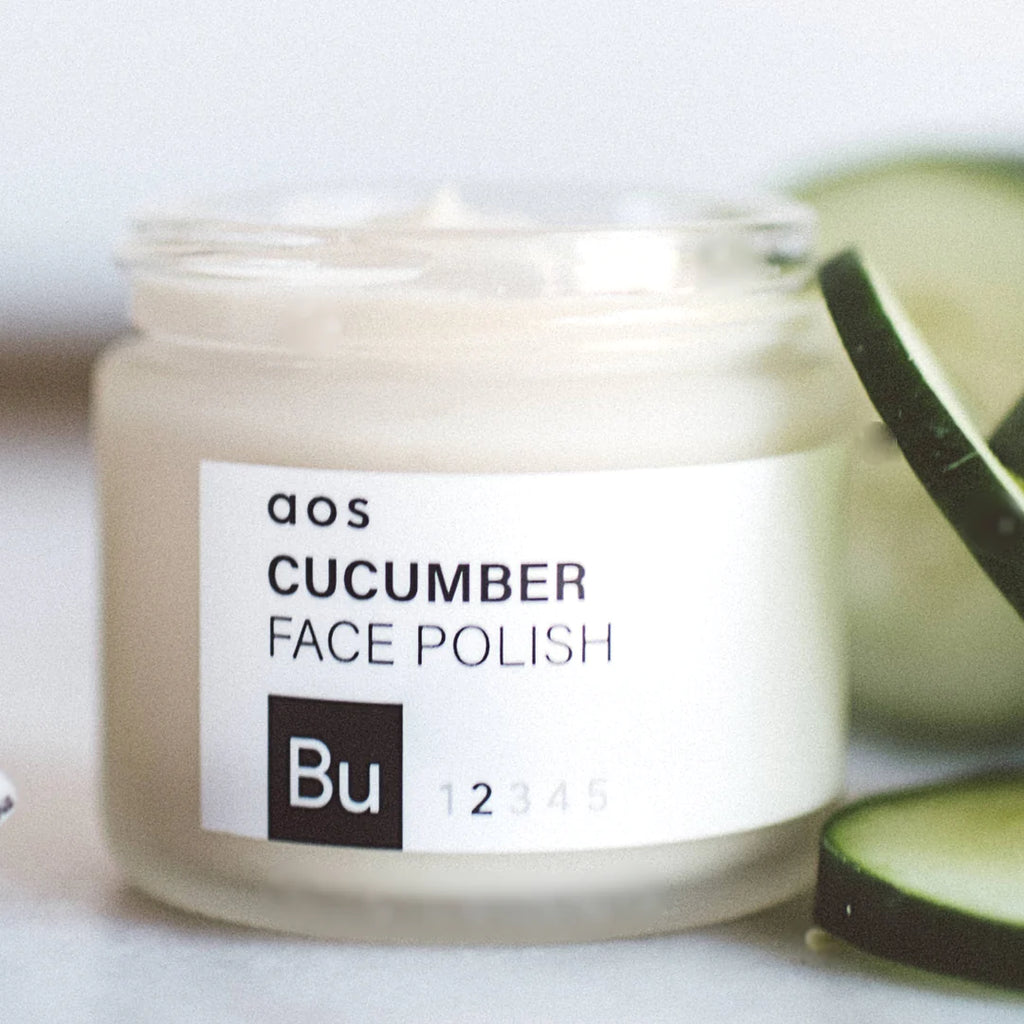 Jar of cucumber face polish with blurred cucumber slices in the background.