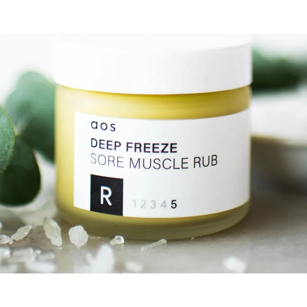 Jar of "qos deep freeze sore muscle rub" with crystals and leaves in the background.