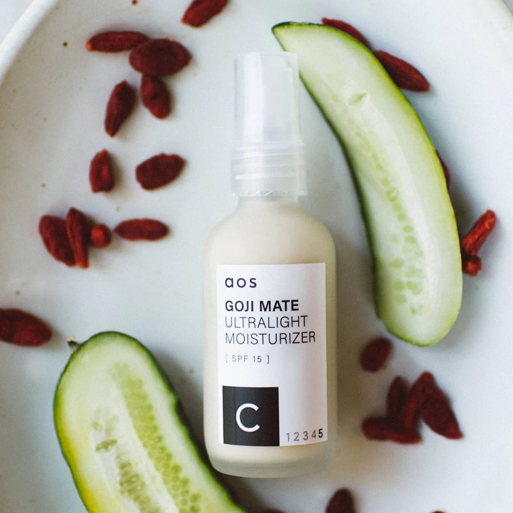 Bottle of goji mate ultralight moisturizer with spf 15 surrounded by cucumber slices and goji berries on a white surface.