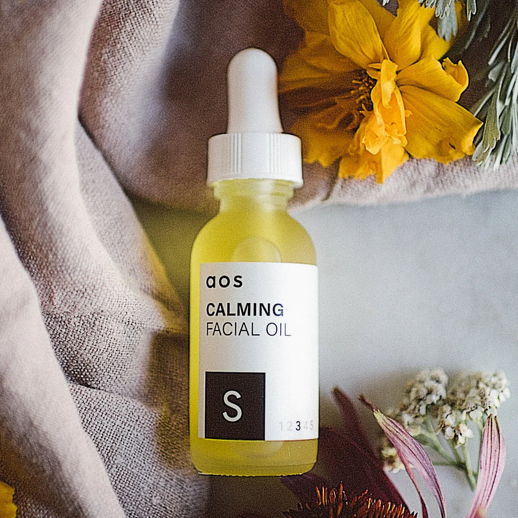 A bottle of calming facial oil surrounded by flowers.