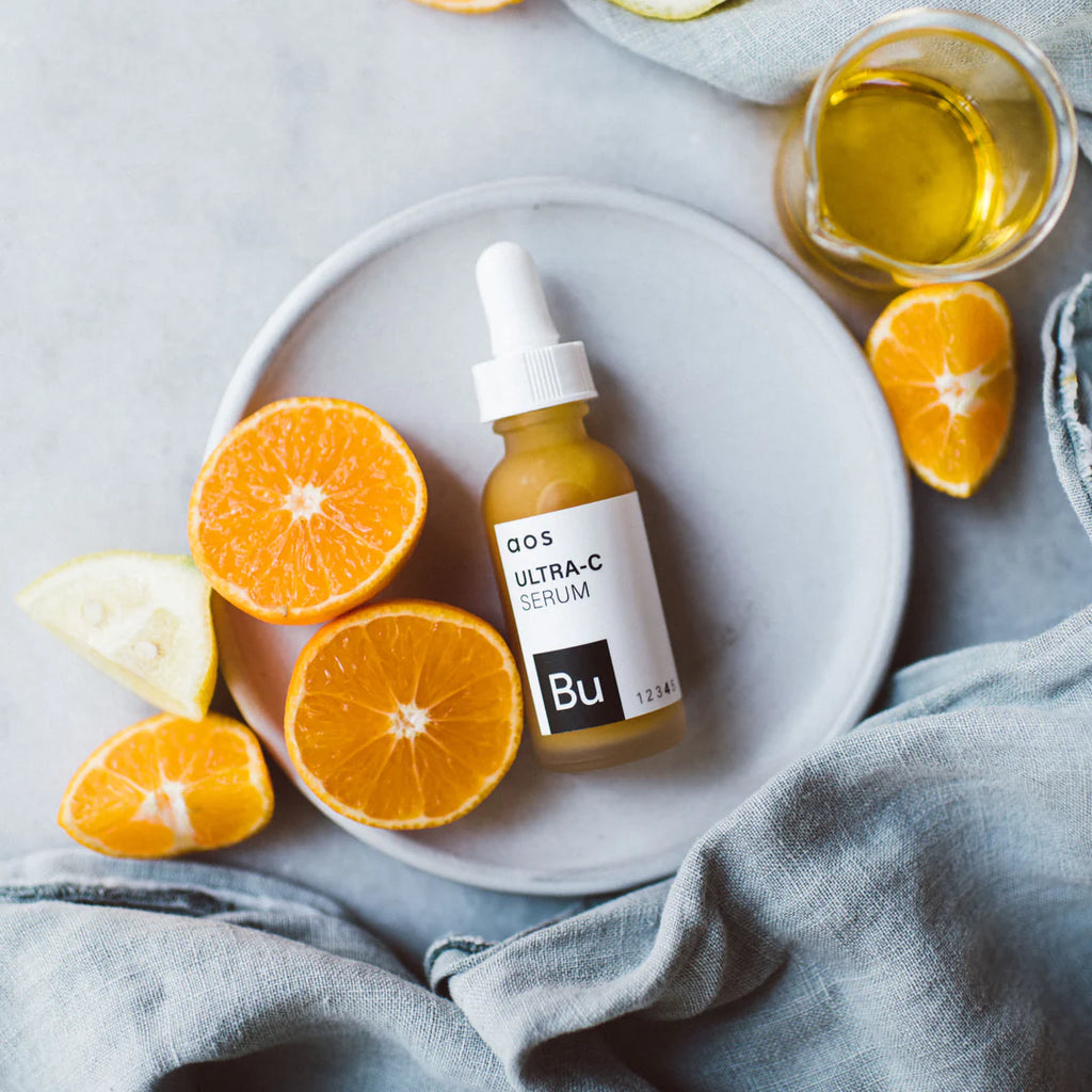 A bottle of ultra-c serum placed beside fresh orange slices on a ceramic plate.