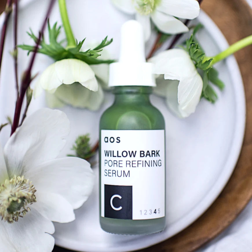 A bottle of willow bark pore refining serum placed on a plate with white flowers around it.