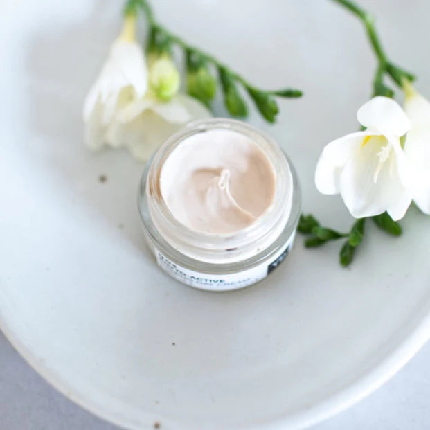 Open jar of cosmetic cream on a plate with white flowers nearby.