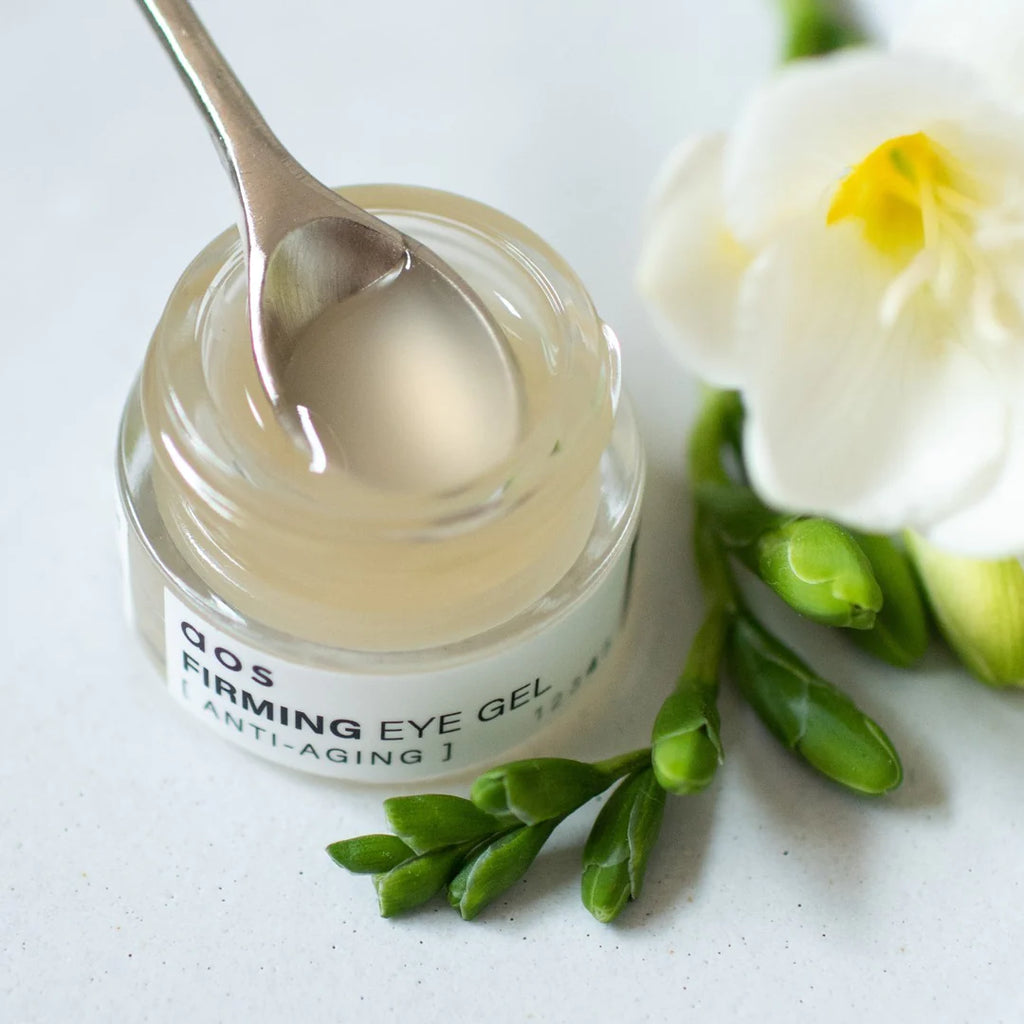A jar of firming eye gel with a spoon and a white flower on a light background.