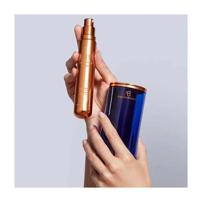A person holding two cosmetic bottles, one bronze and one blue, against a plain background.