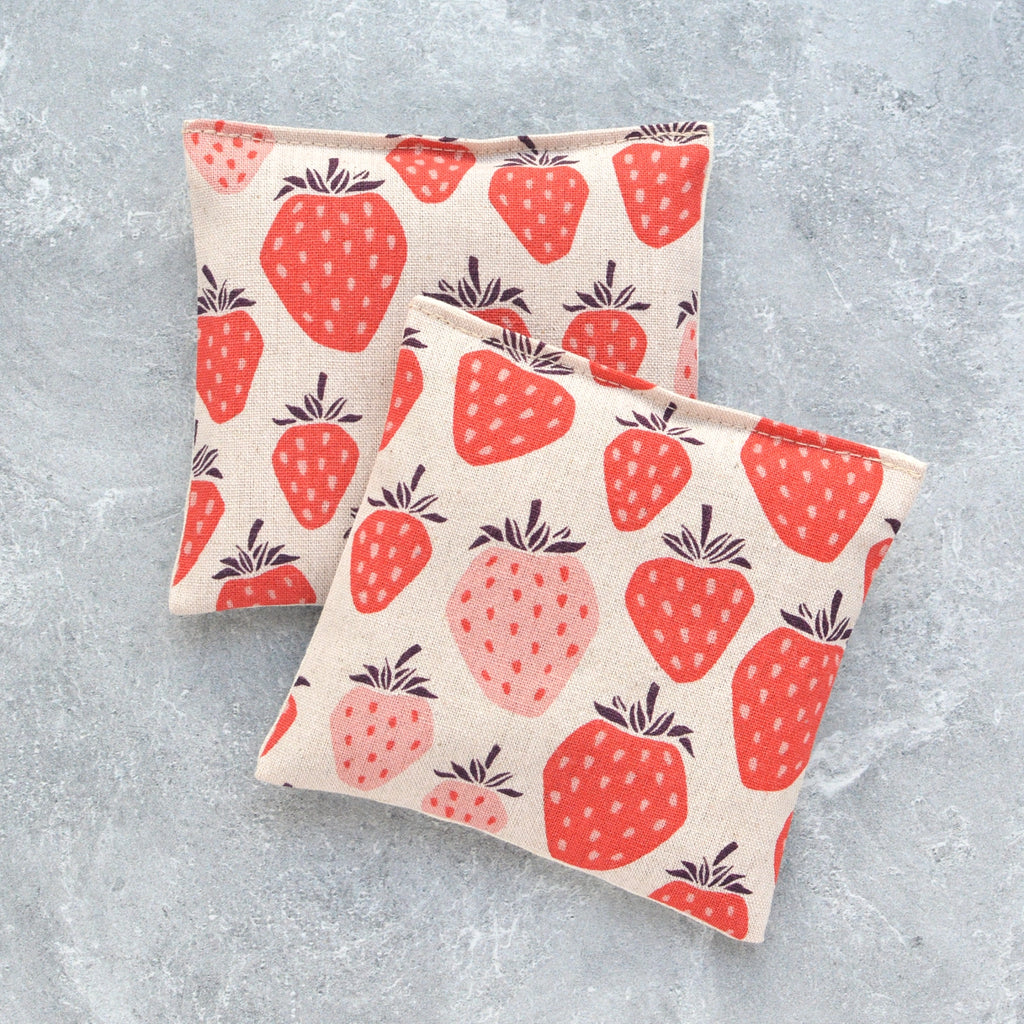 Two fabric pouches with strawberry patterns on a textured grey background.