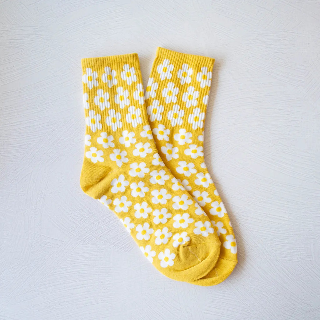 A pair of yellow socks with white floral patterns laid out flat on a light-colored surface.