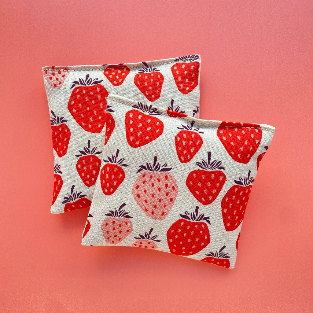 Two pouches with strawberry patterns on a pink background.