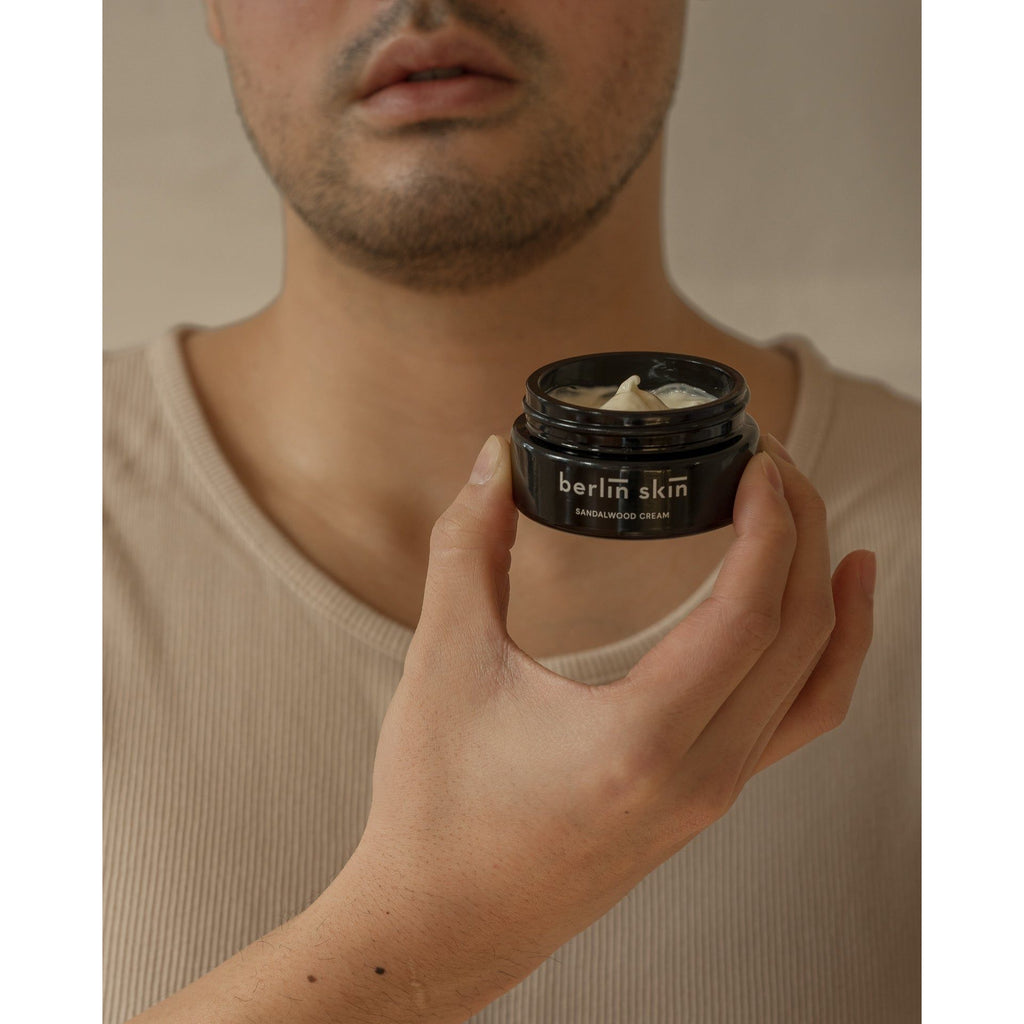 A person holding a jar of berlin skin sandalwood cream.