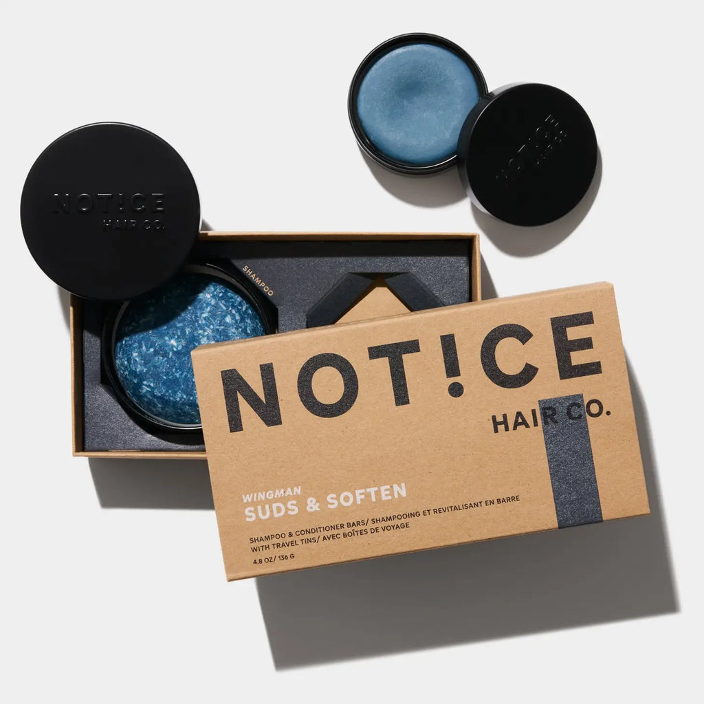 Hair care products from notice hair co. including a "wingman suds & soften" shampoo bar and a small container of blue styling balm, arranged neatly next to their packaging.