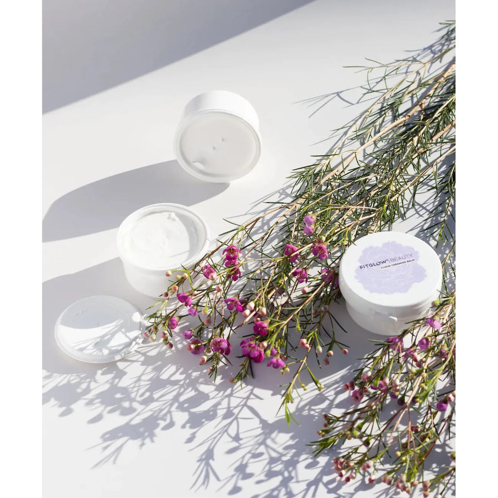 Open skincare jars amidst delicate pink flowers and greenery, bathed in natural light.