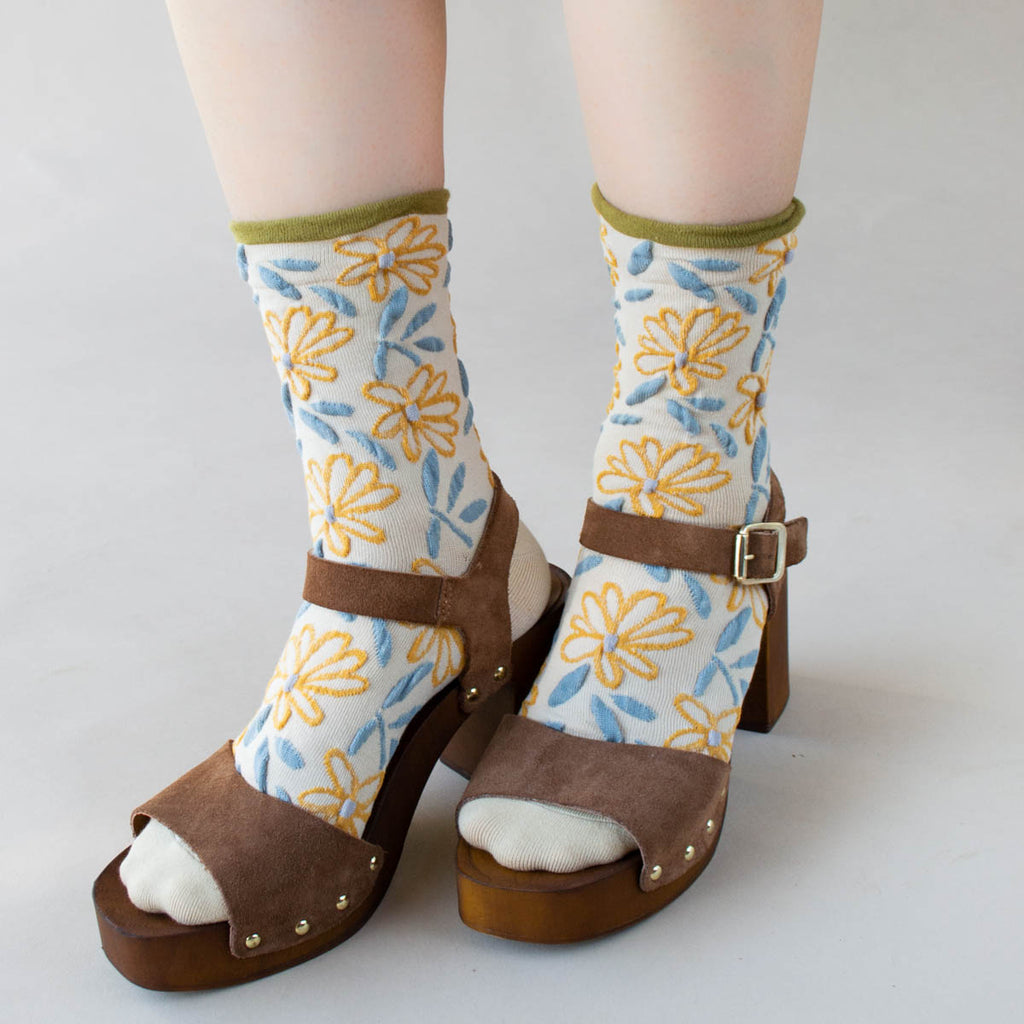 Person wearing floral socks and brown platform sandals.