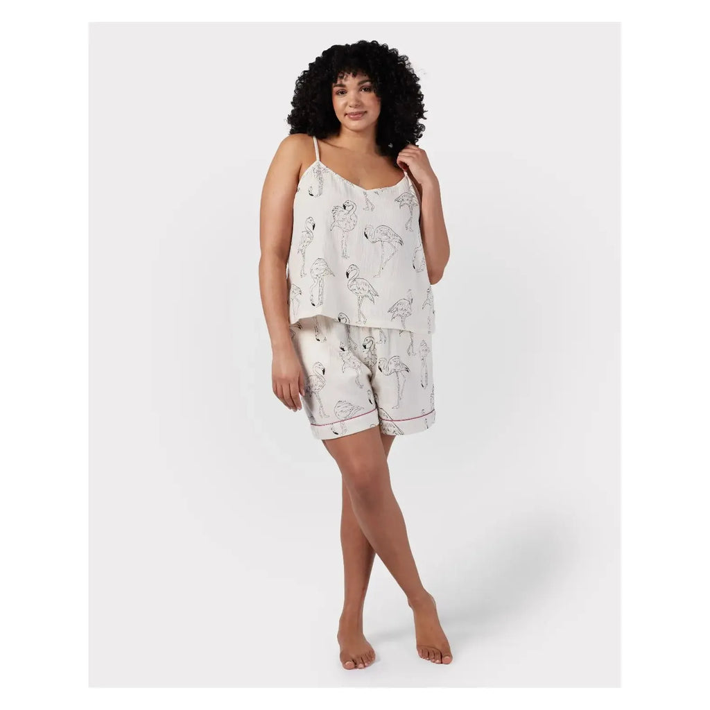 A person with curly hair wearing a white Chelsea Peers Cotton Cheesecloth Flamingo Sketch Print Cami Short Pajama Set, adorned with a whimsical mushroom and flamingo print, stands barefoot against a plain white background.
