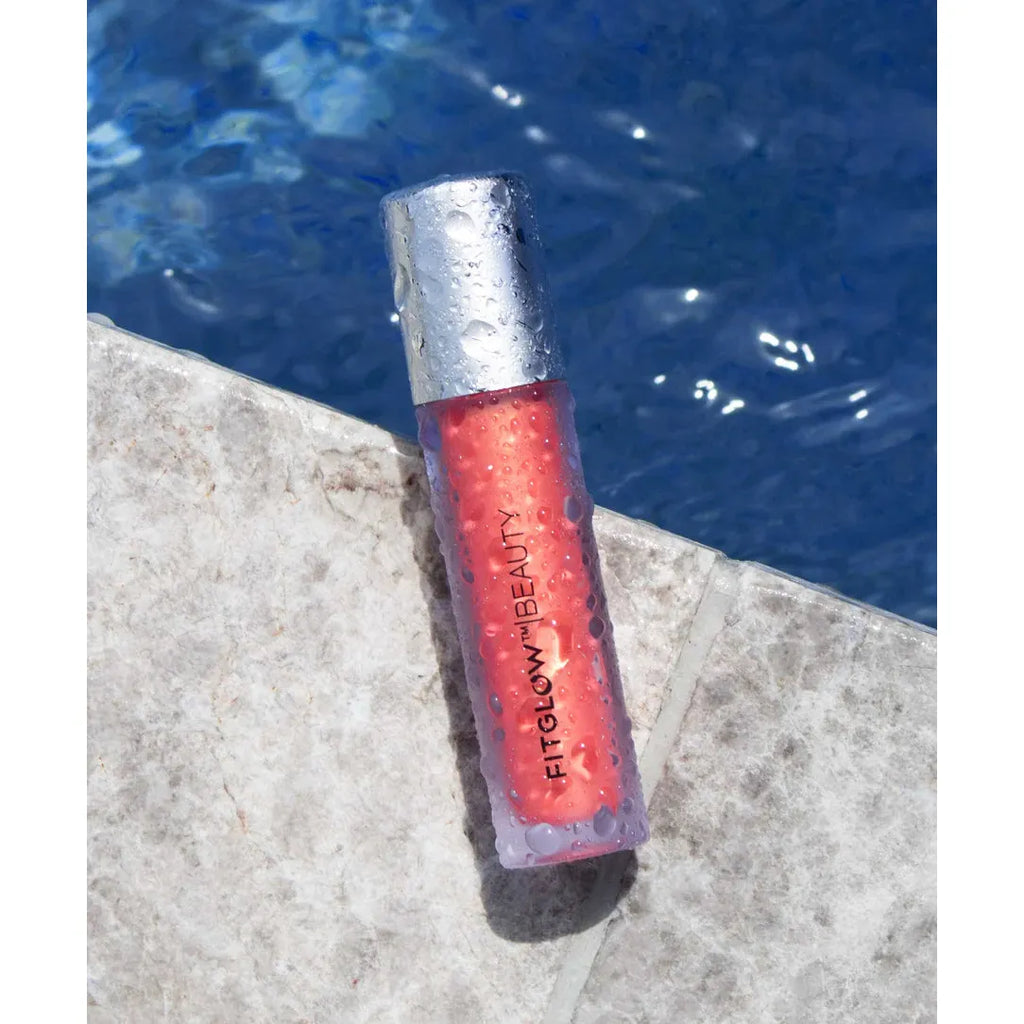 A tube of fenty beauty lip gloss resting on a poolside edge with water in the background.