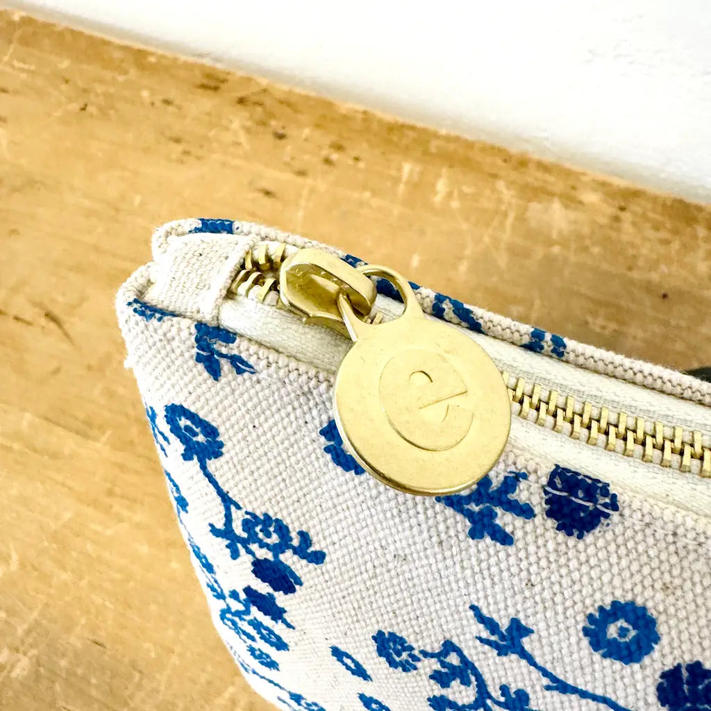 A close-up of a fabric pouch with blue floral print and a gold-tone zipper.