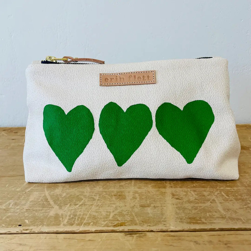 White canvas pouch with three green hearts and a designer label.
