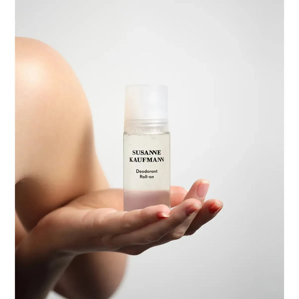 A close-up of a hand holding a bottle of Susanne Kaufmann Deodorant Roll On with a neutral backdrop.