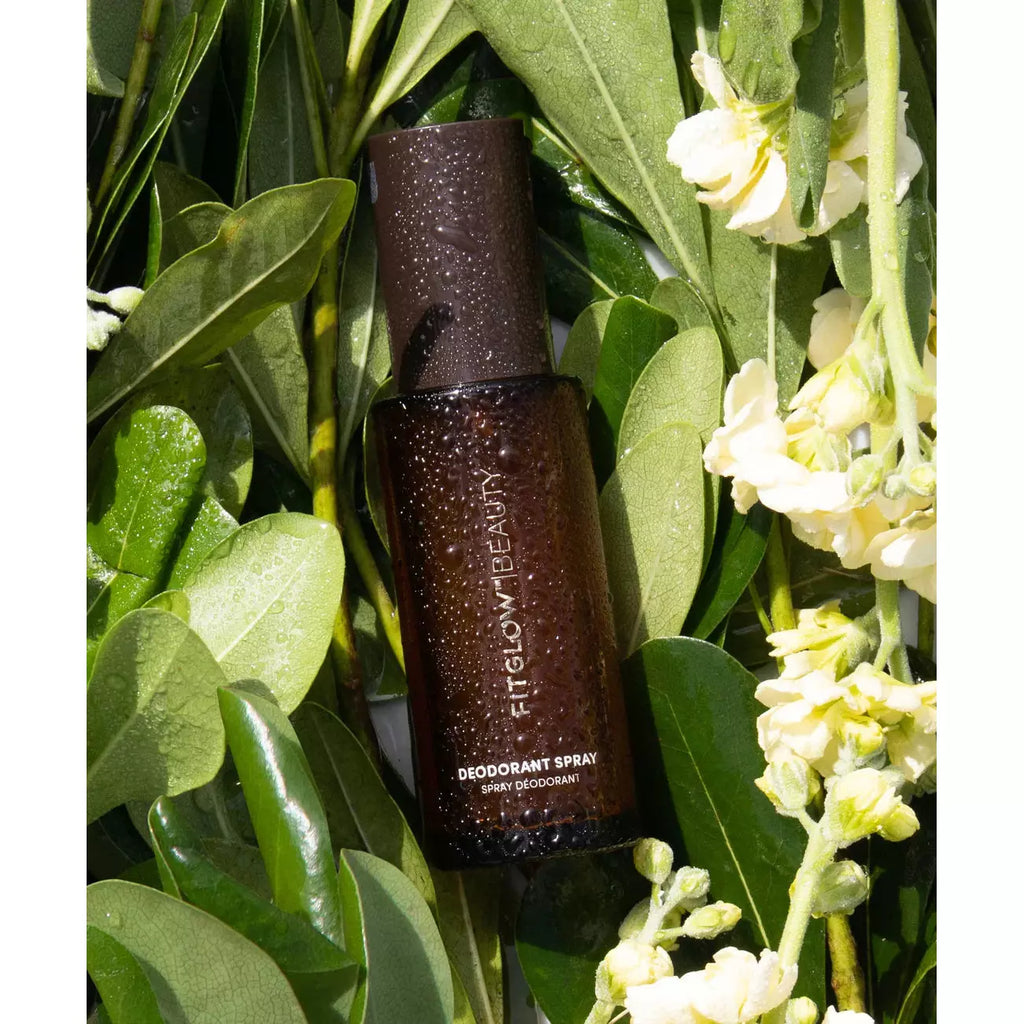 Bottle of deodorant spray nestled among green leaves and white flowers.
