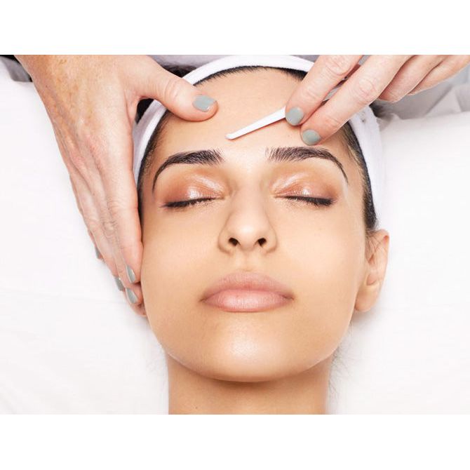 A person receiving a facial treatment with tweezers being used near the brow area.