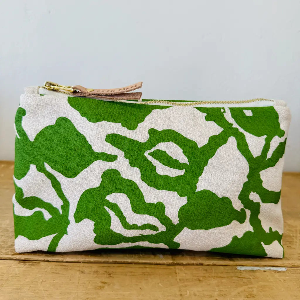 Green and white patterned fabric pouch with a zipper on a wooden surface.