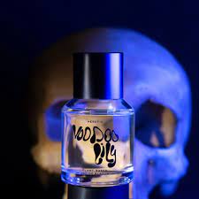 A bottle of "voodoo lily" perfume in front of a human skull with a blue background.