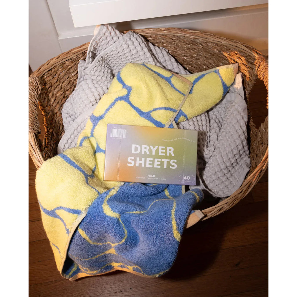 A box of dryer sheets placed on top of folded towels in a wicker basket.