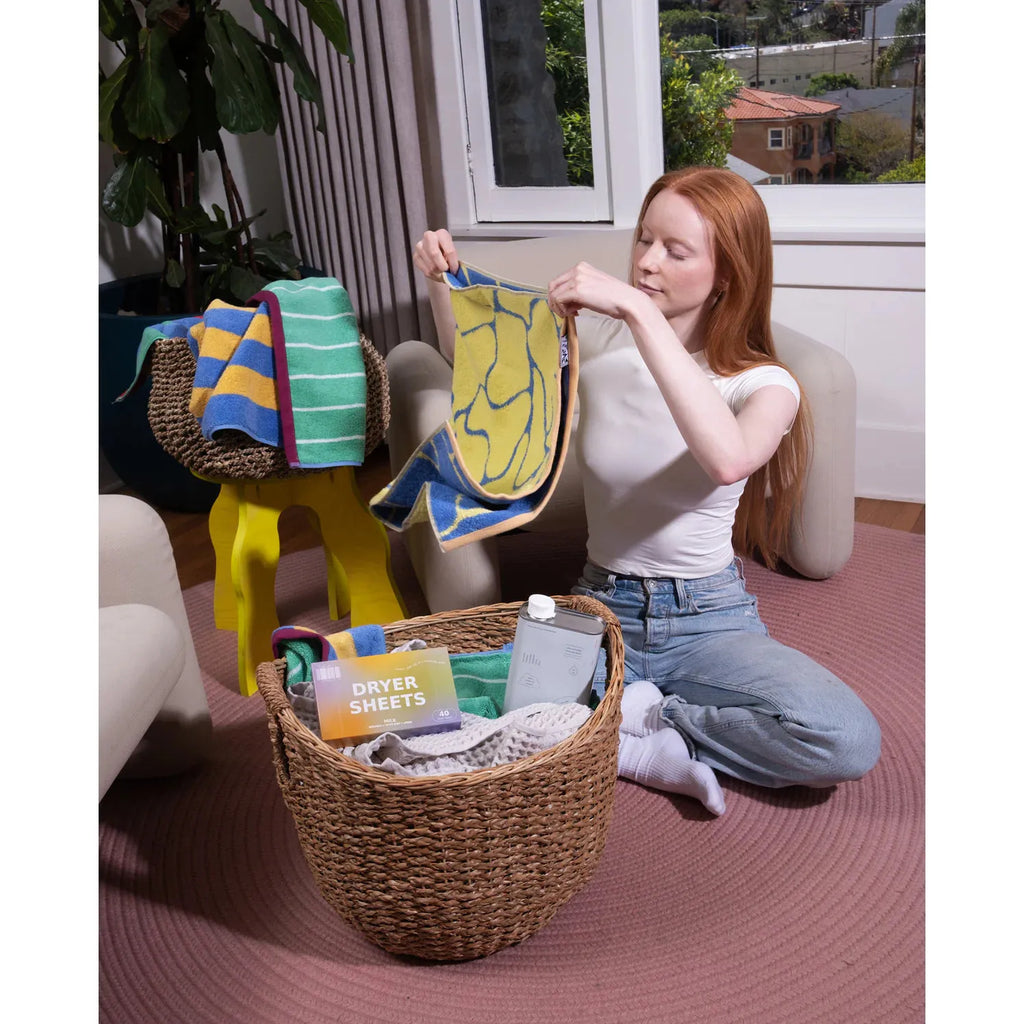 A woman sitting on the floor folding laundry next to a wicker basket.